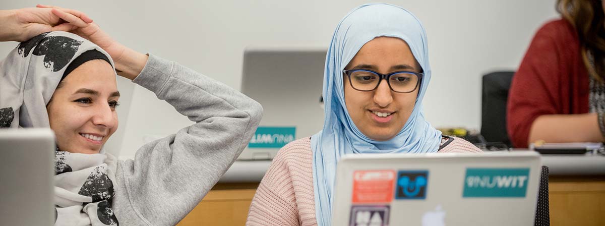 Two women look at a laptop during class